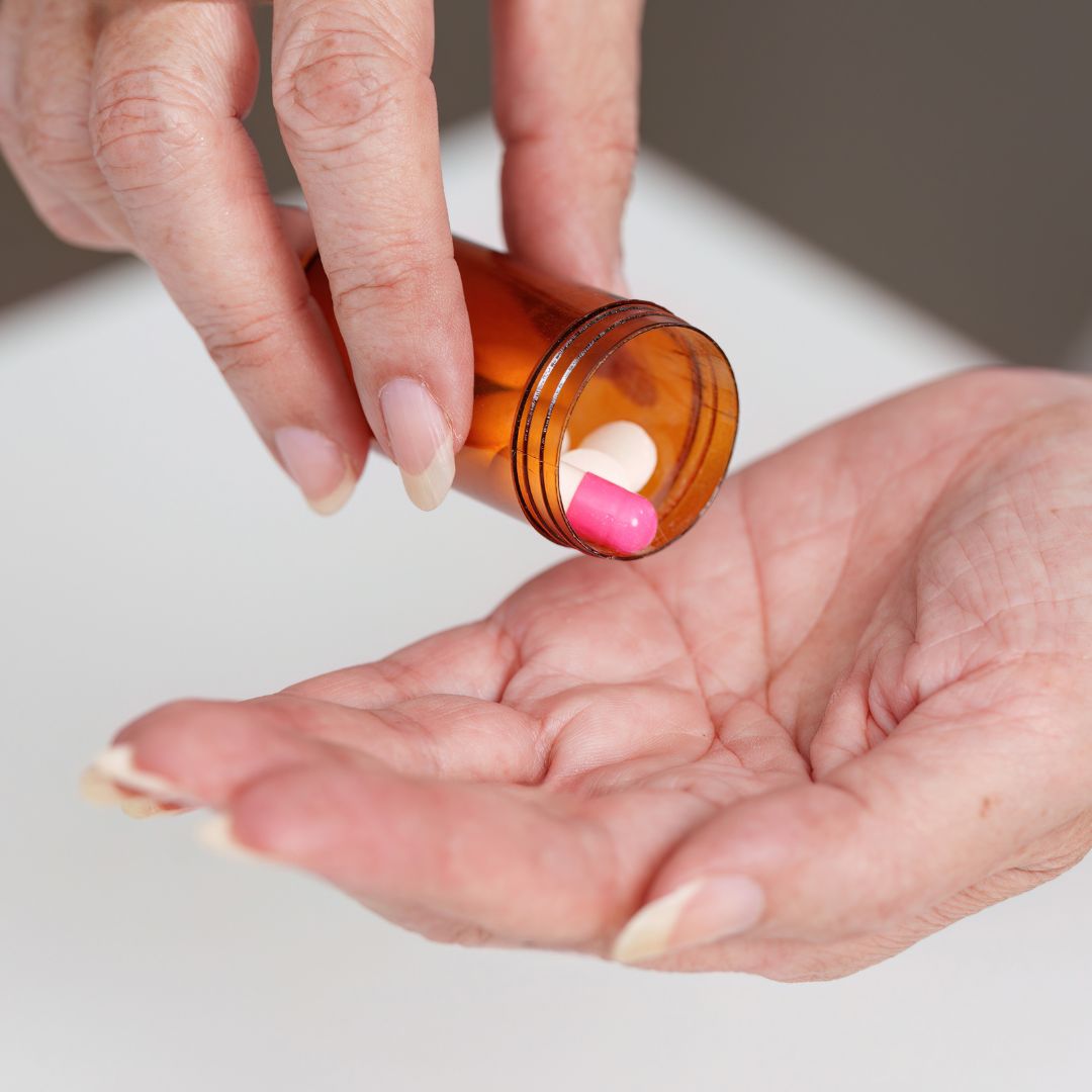 Elderly hands pouring pink and white supplement pills from medicine bottle