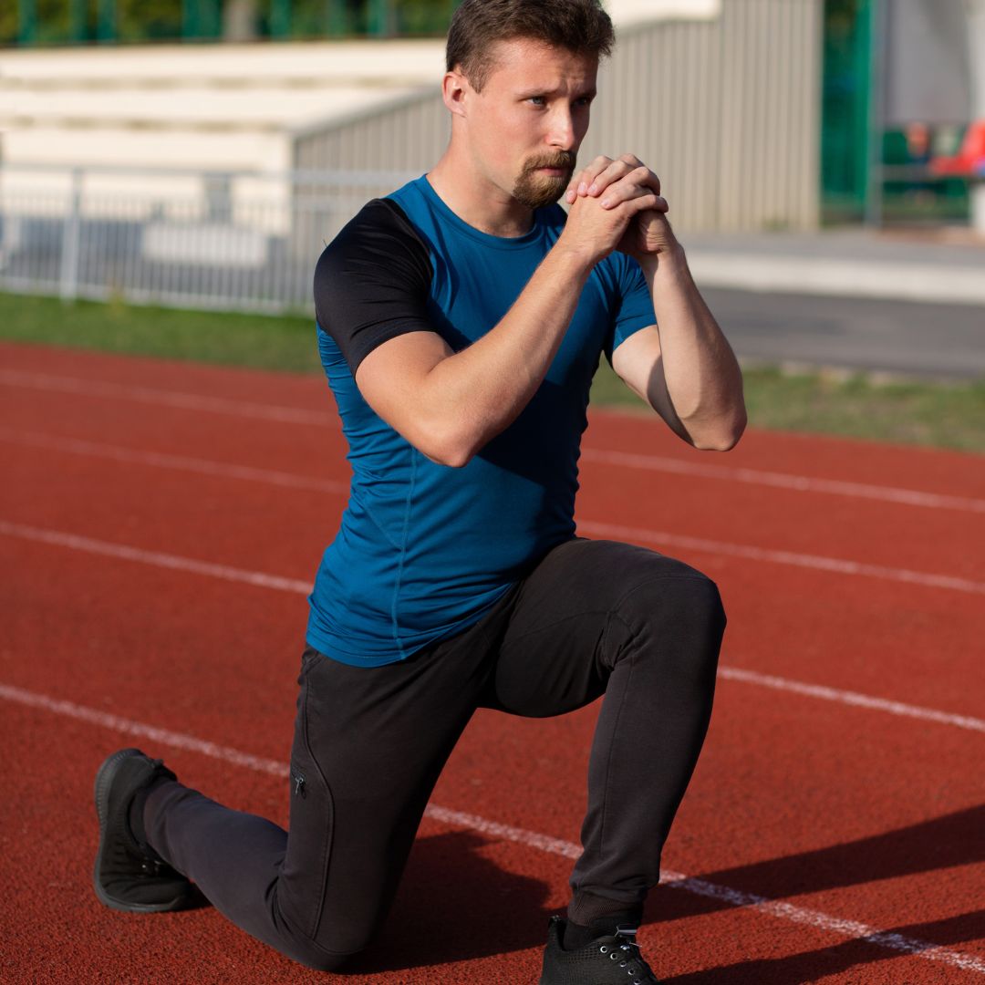 Athletic man doing lunge stretch on red outdoor running track