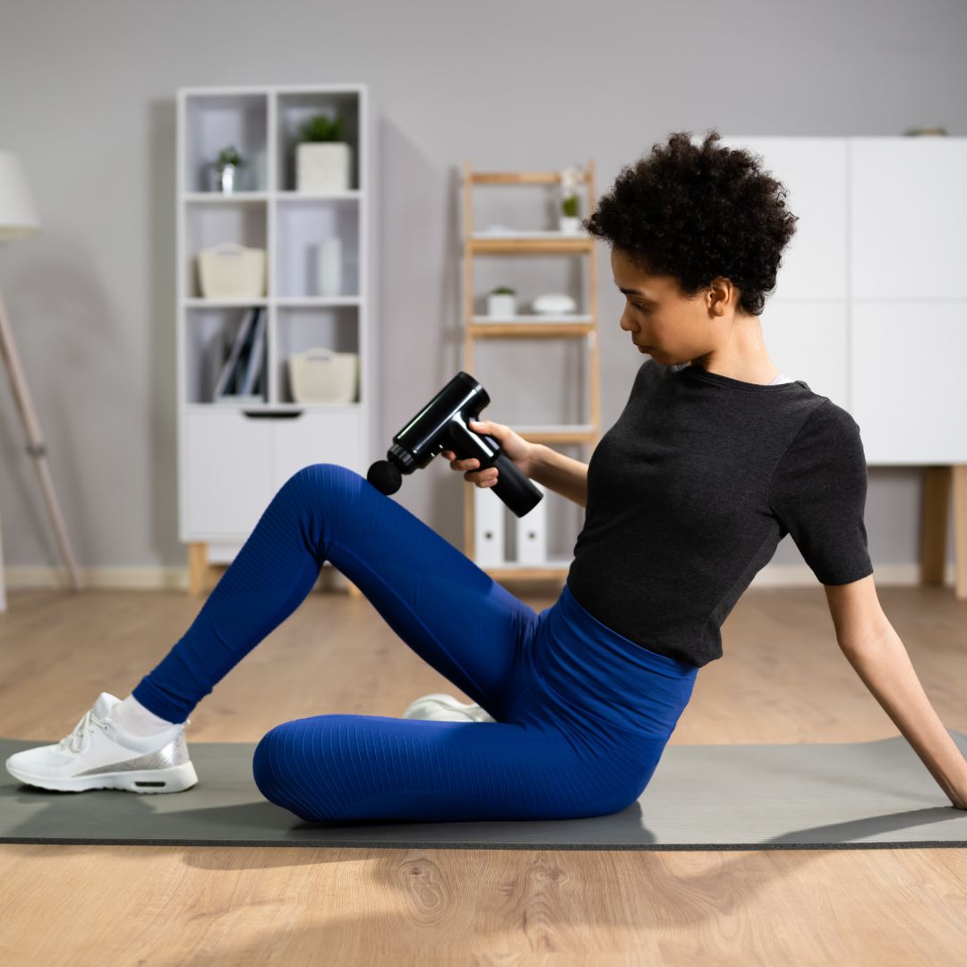Young woman using massage gun on leg for muscle recovery after workout session