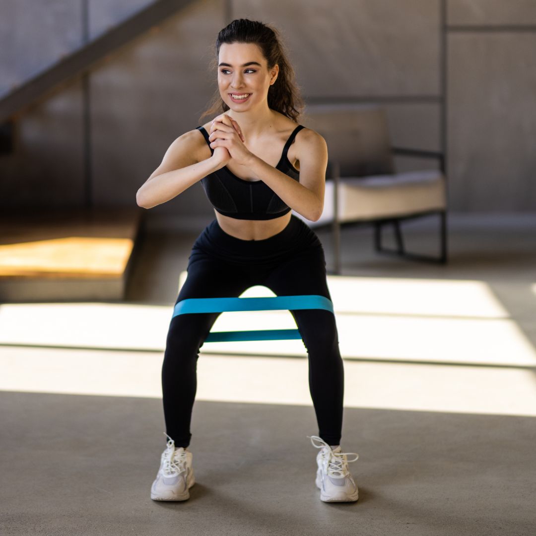 Fit woman performing squat exercise with blue resistance band in modern gym studio